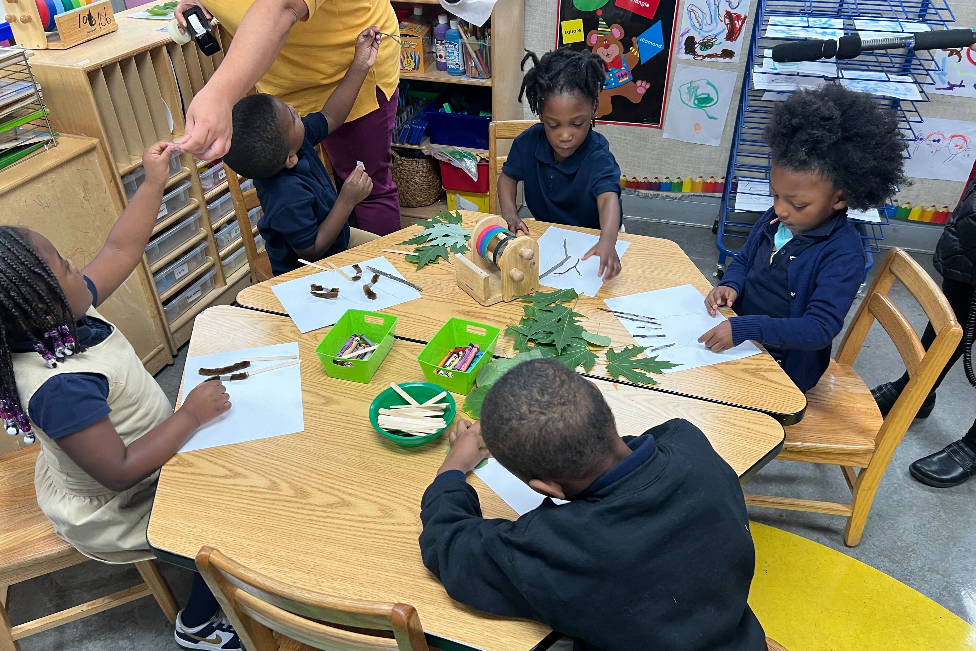 A woman in yellow helps a group of young students in blue shirts at a table.