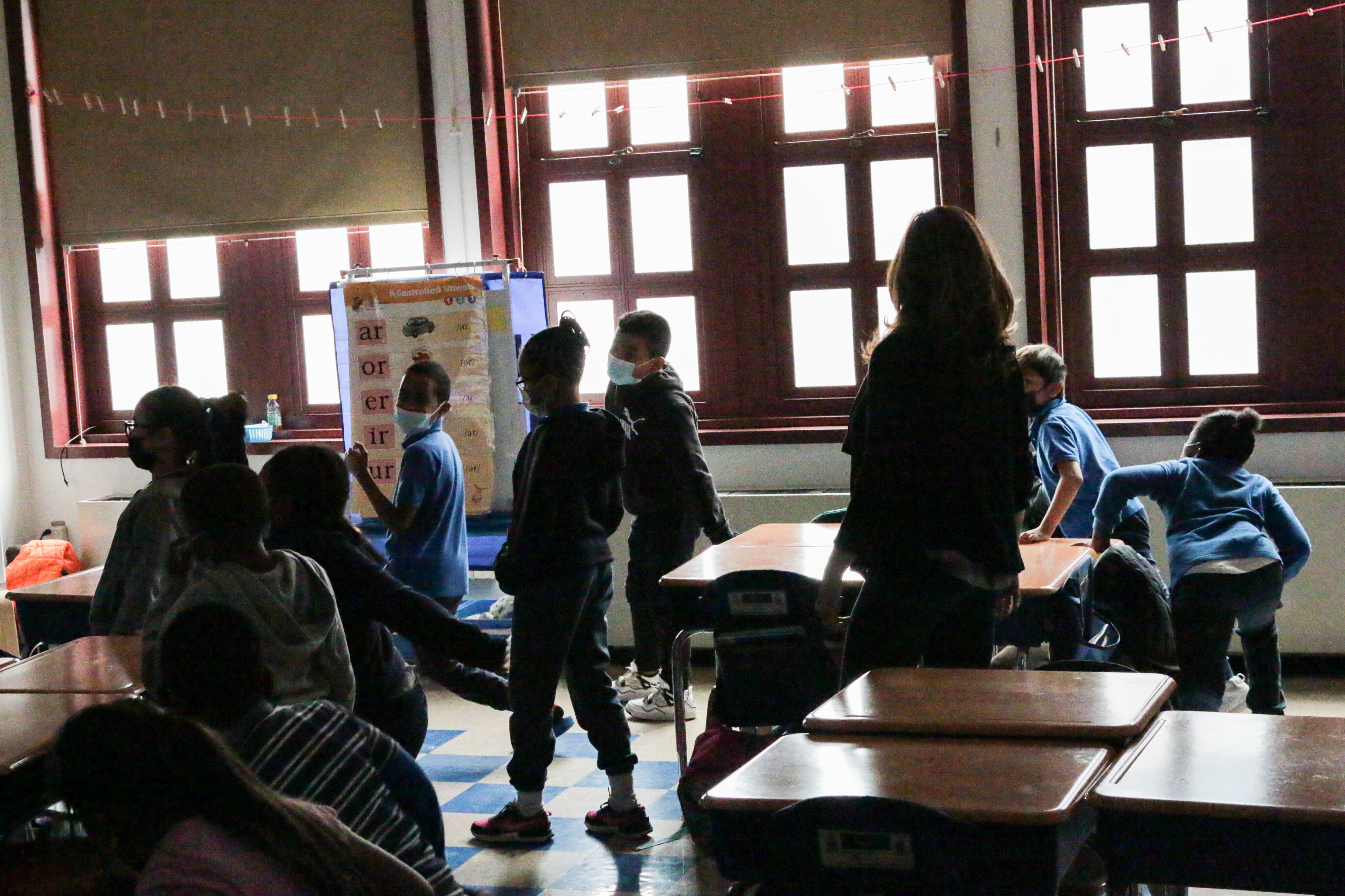 Some students are standing, while others are sitting in a classroom.