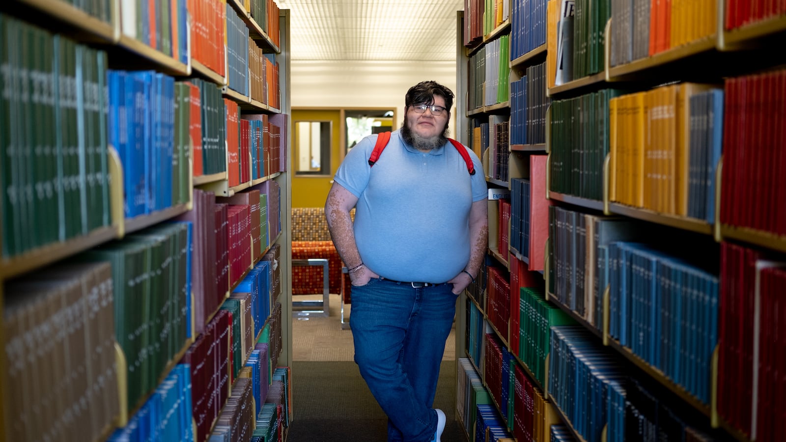 Reginaldo Haro-Flores lleva una camisa azul; está parado en la biblioteca entre estanterías.