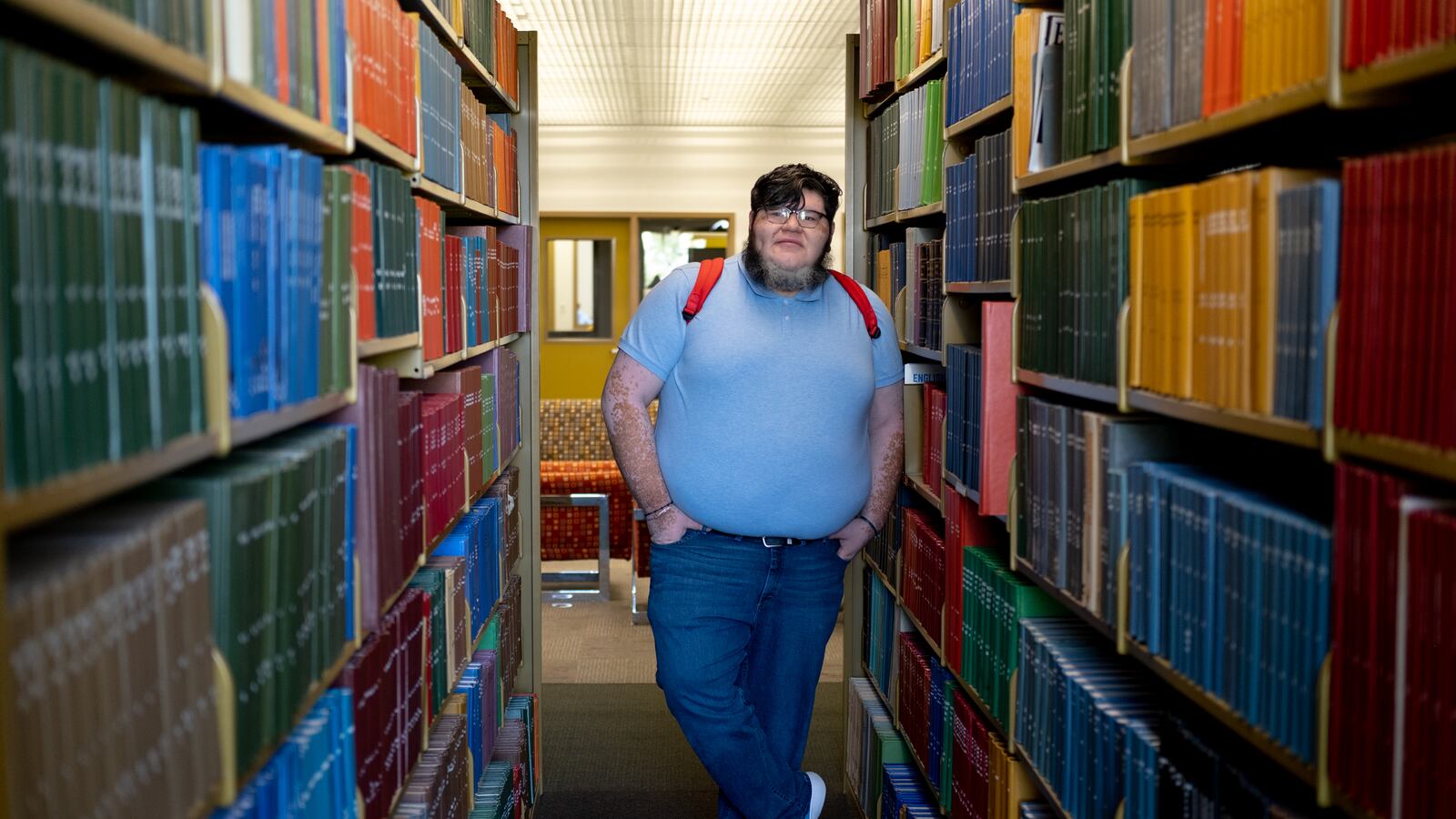 Reginaldo Haro-Flores lleva una camisa azul; está parado en la biblioteca entre estanterías.