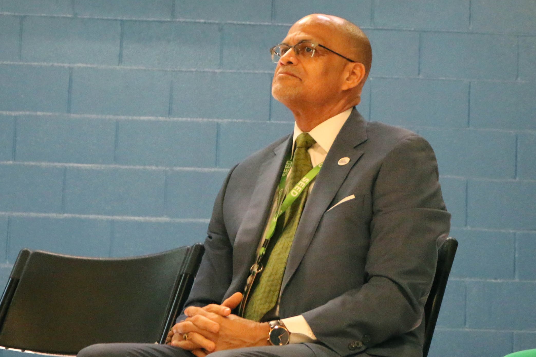 A man in a dark suit sits with his hands in his lap.