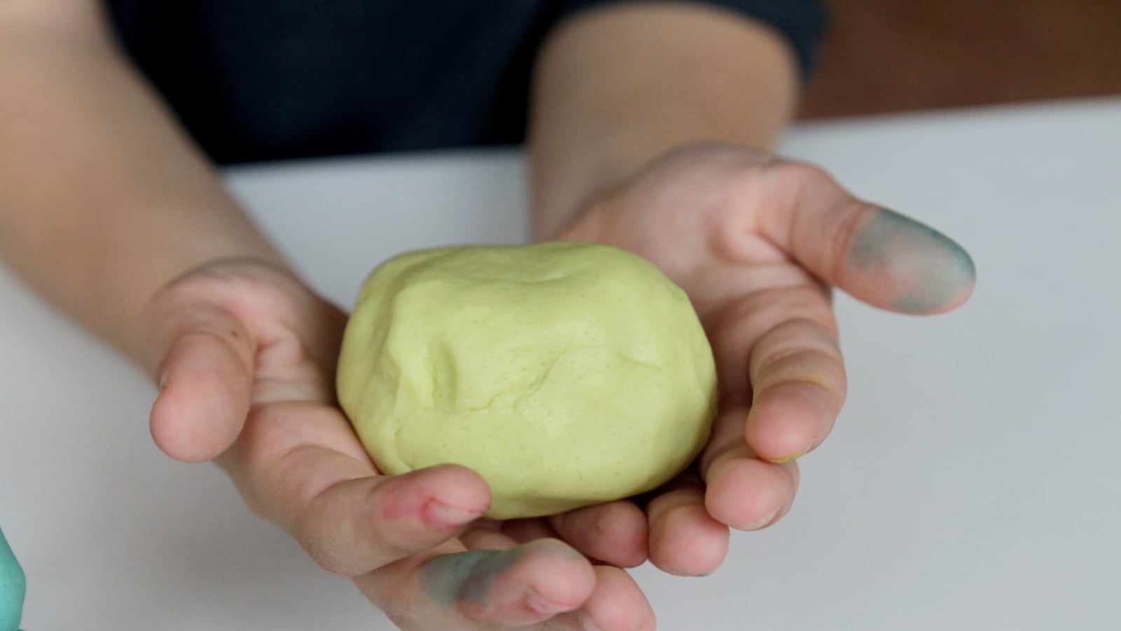 A child’s hands hold a yellow ball of playdough.