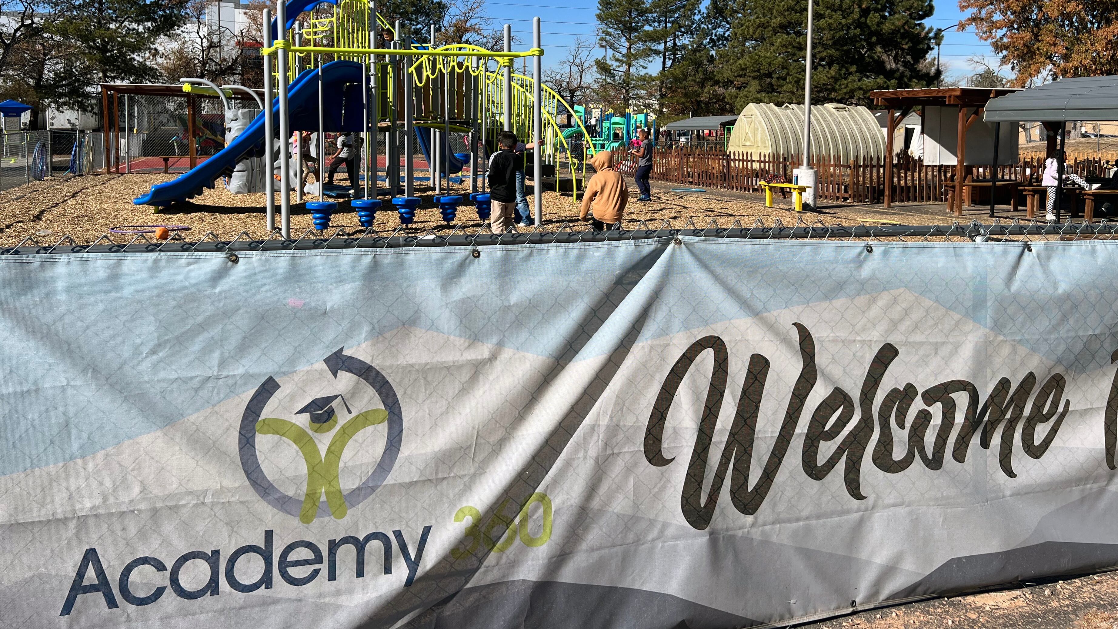 A banner with the words "Academy 360" and "Welcome" in the foreground with young students playing at a playground in the background.