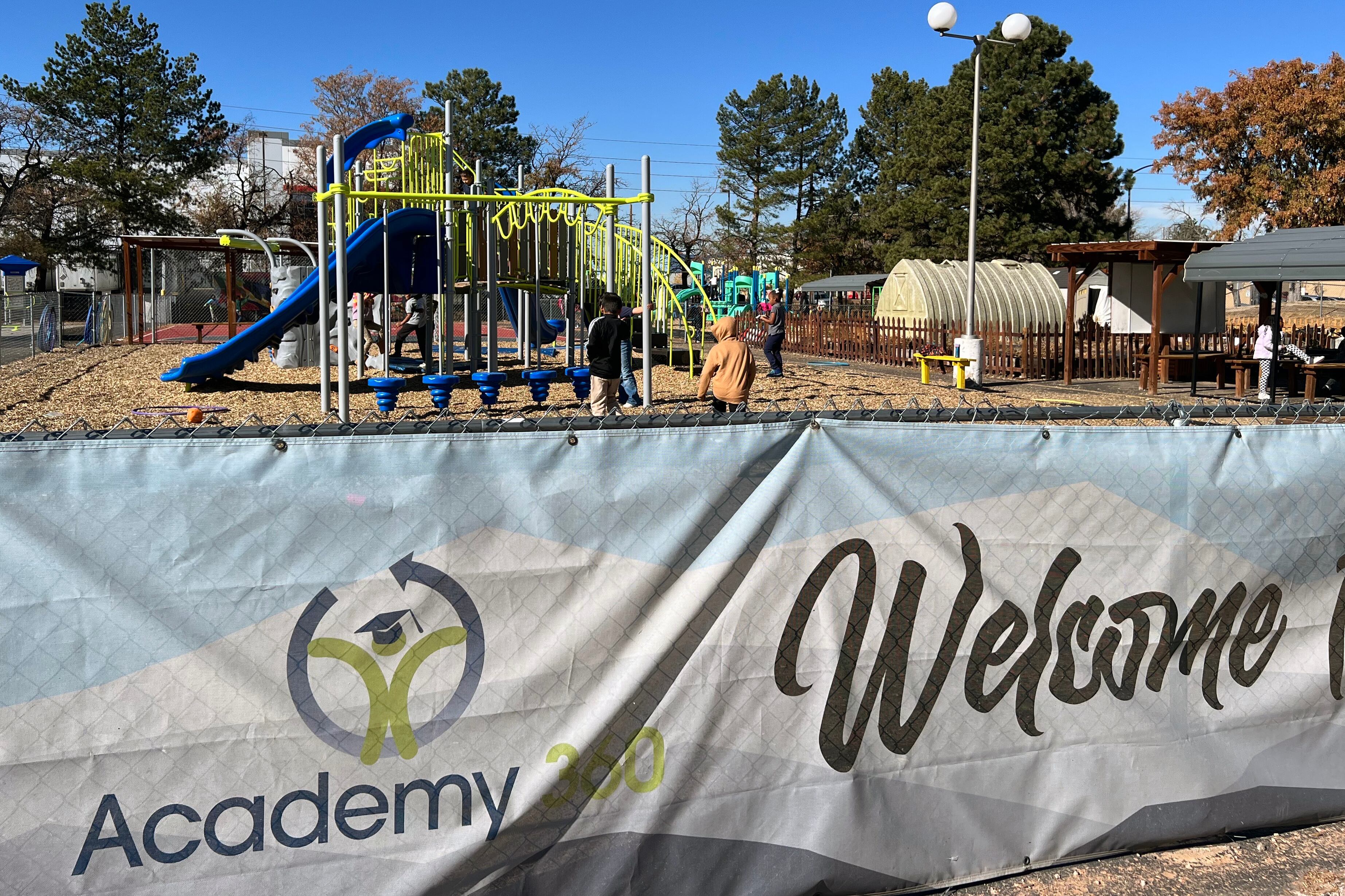 A banner with the words "Academy 360" and "Welcome" in the foreground with young students playing at a playground in the background.