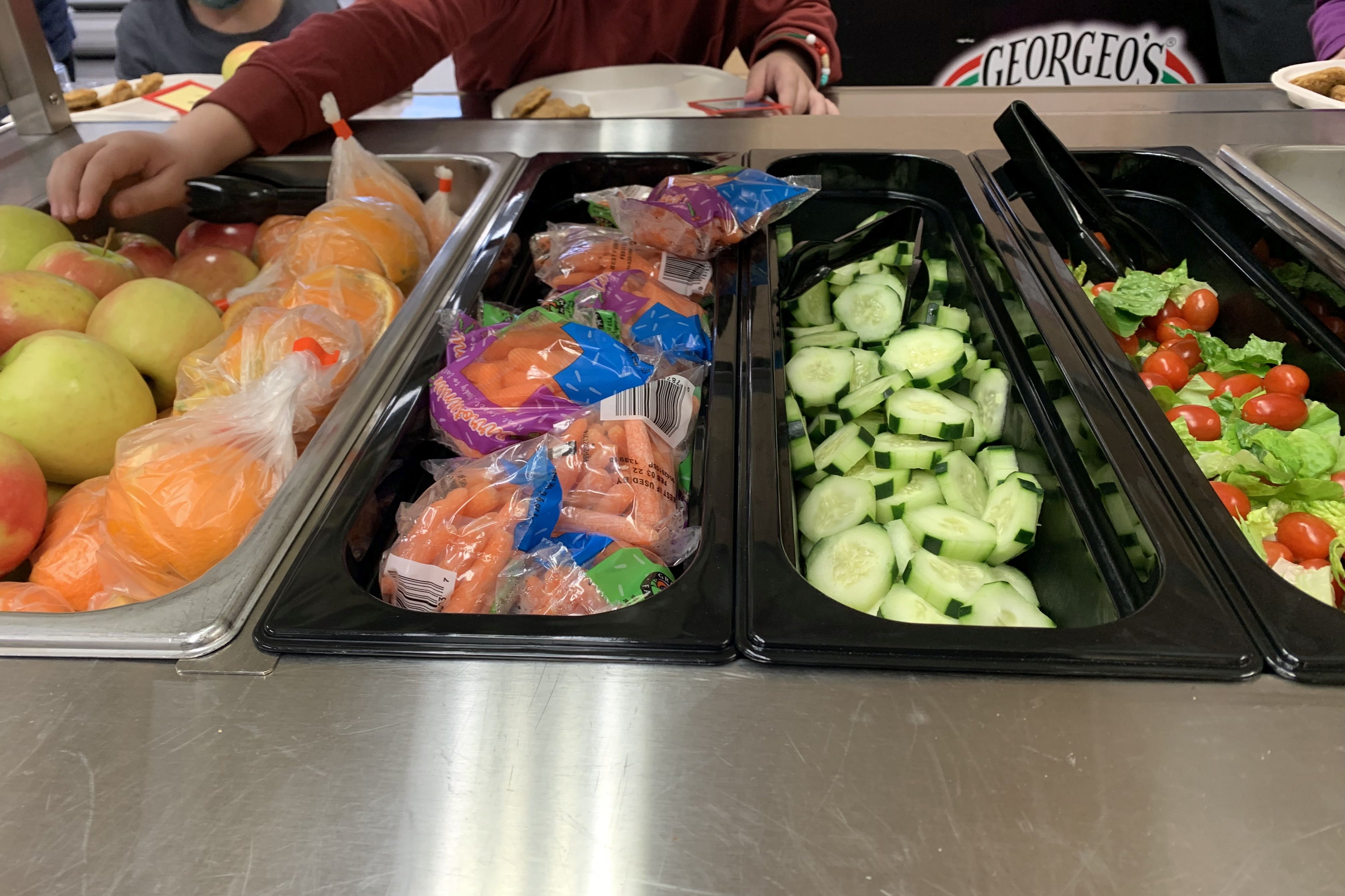 An elementary school student reaches for an apple on a school lunch line.