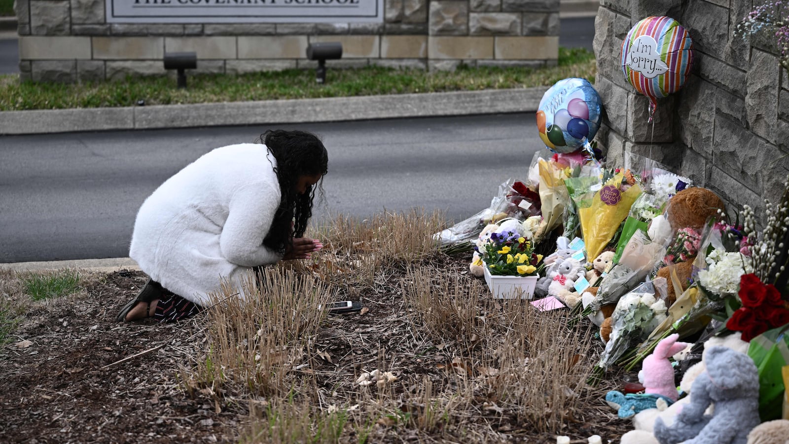 A woman bends down in front of a row of flower bouquets against a stone wall.