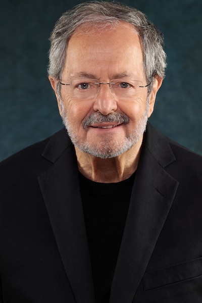 A headshot of a man with glasses and dark clothes.