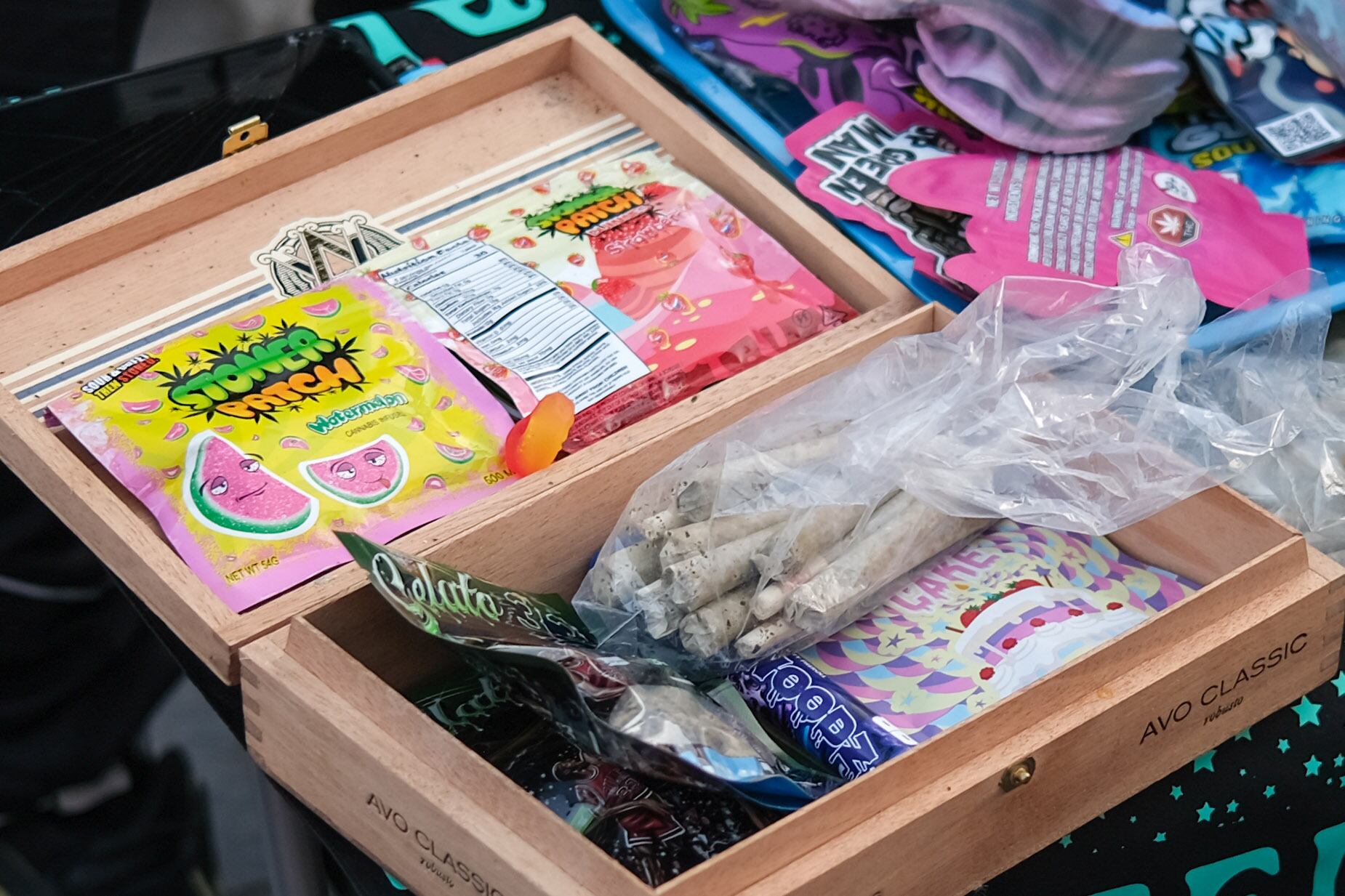 A wooden box full of pre-rolled joints and colorful THC infused gummy candy packages.