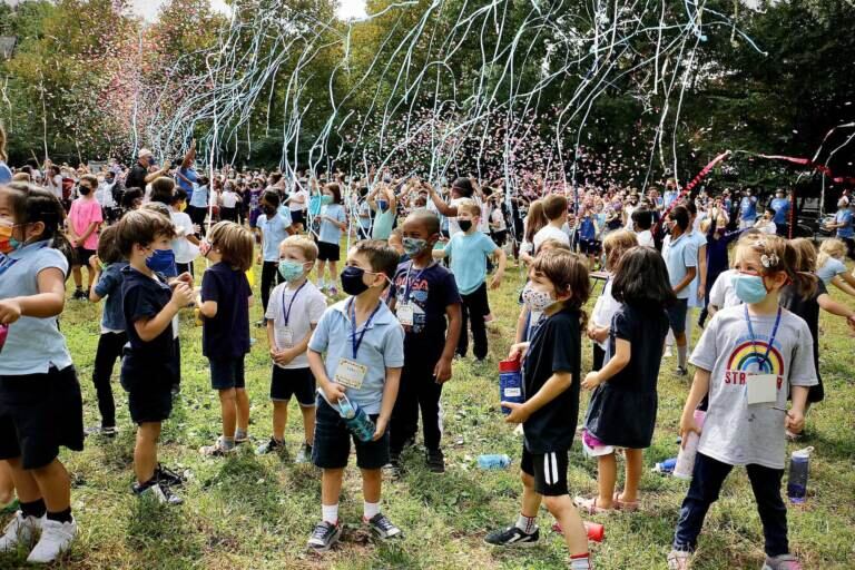 Students in masks celebrate outside at Penn Alexander after being announced as a National Blue Ribbon School. Streamers are in the air above the students.