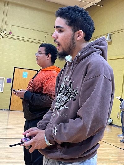 A boy in a gray sweatshirt holds a piece of equipment in a gymnasium.