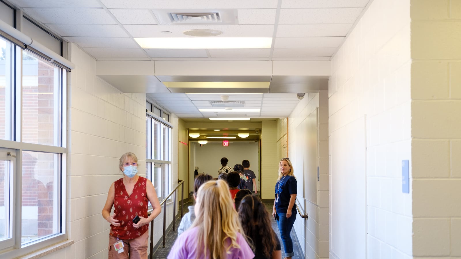 Elementary students and faculty walk down a white hallway on the first day of school.