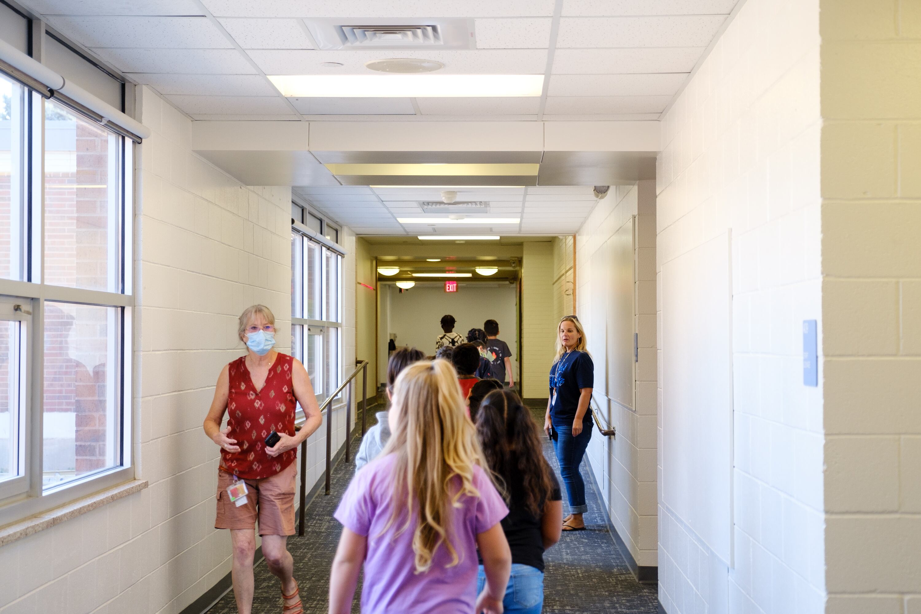 Elementary students and faculty walk down a white hallway on the first day of school.
