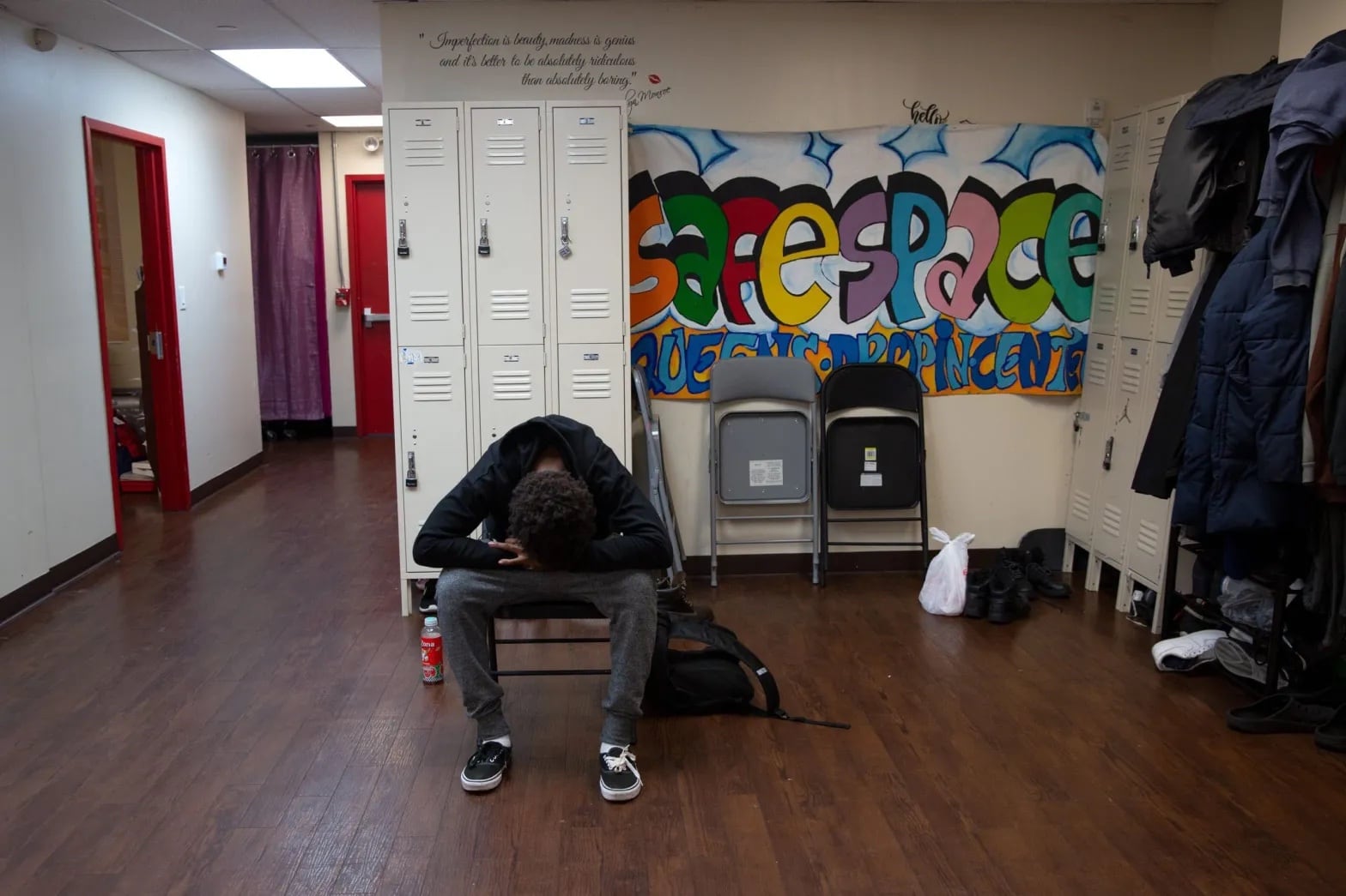 A teen sits in front of lockers with his head in his lap.