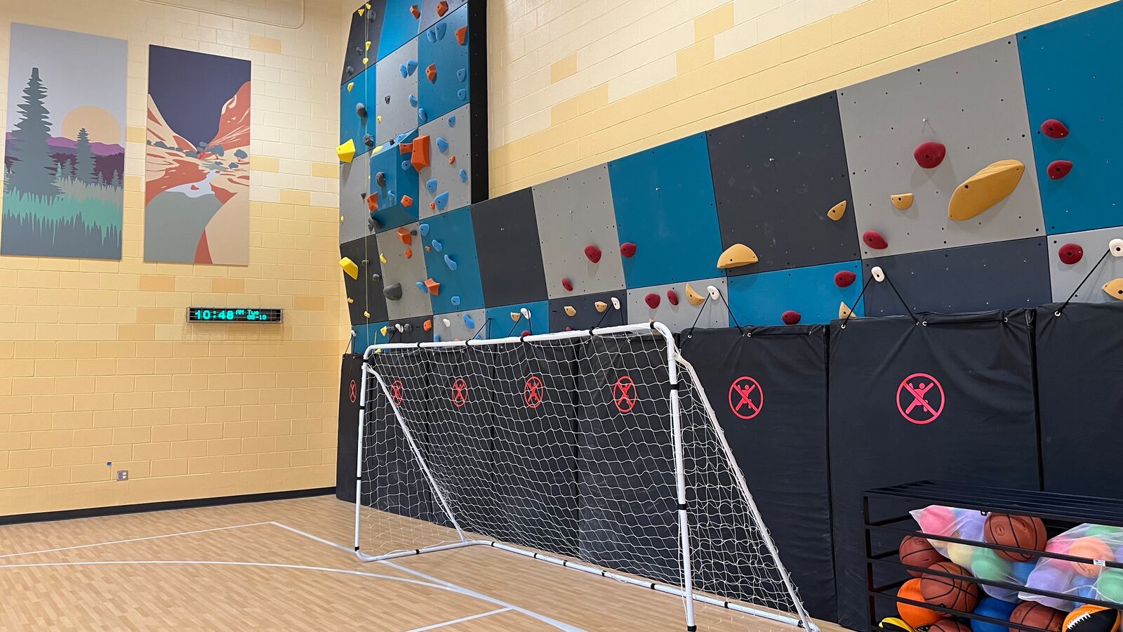 A multicolored climbing wall in the corner of a gymnasium.