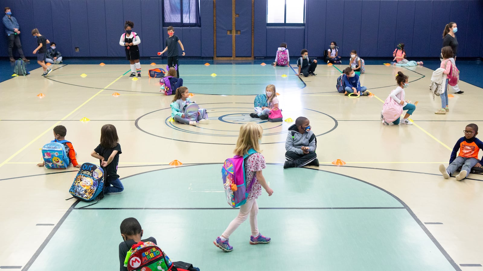 Students line up on colored dots by class in the school gym to wait for their rides after dismissal.