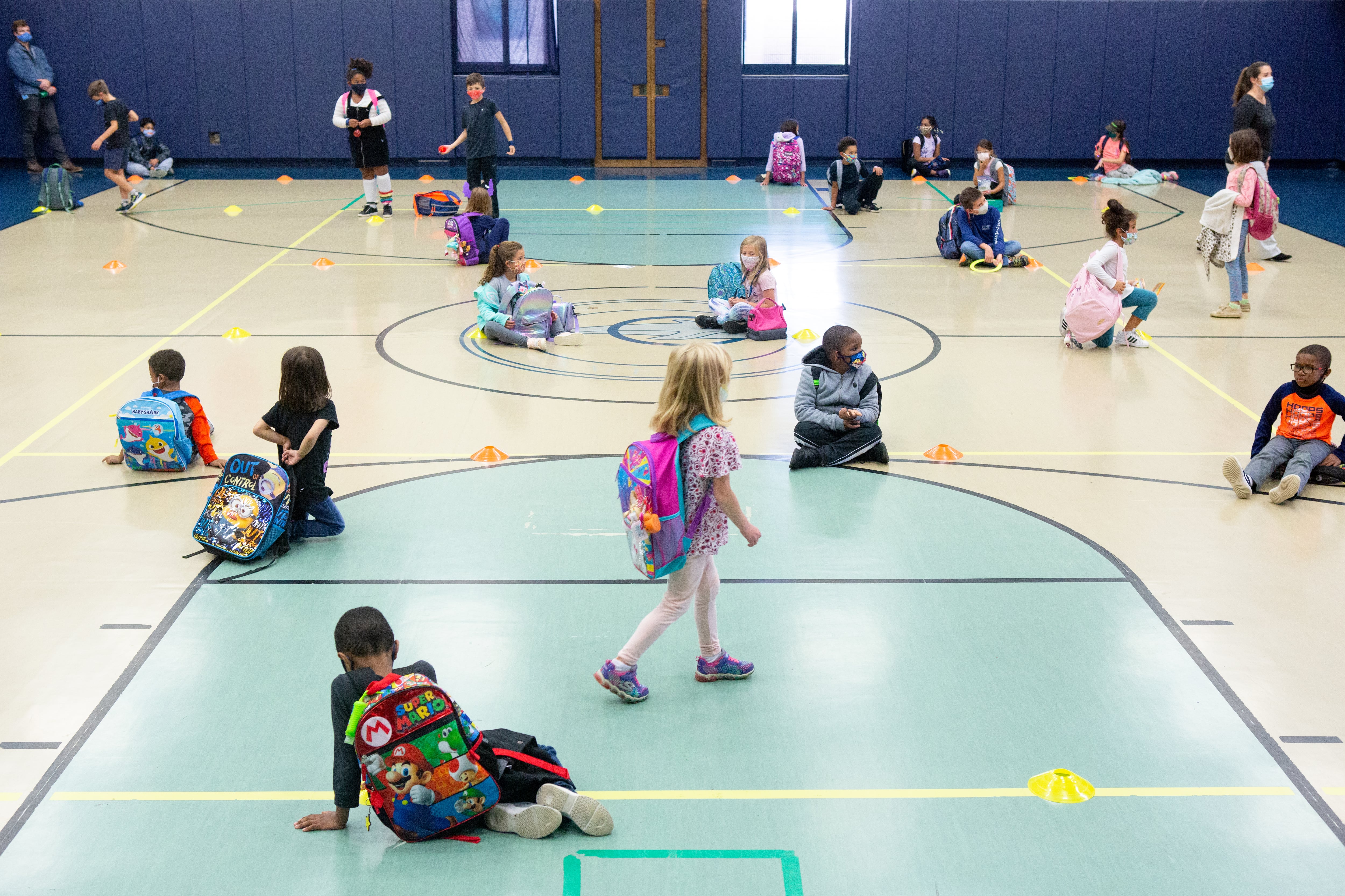 Students line up on colored dots by class in the school gym to wait for their rides after dismissal.