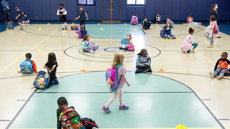 Students line up on colored dots by class in the school gym to wait for their rides after dismissal.