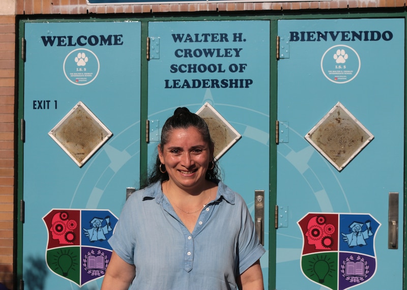 A photograph of a woman in a blue shirt stands in front of a blue set of doors.