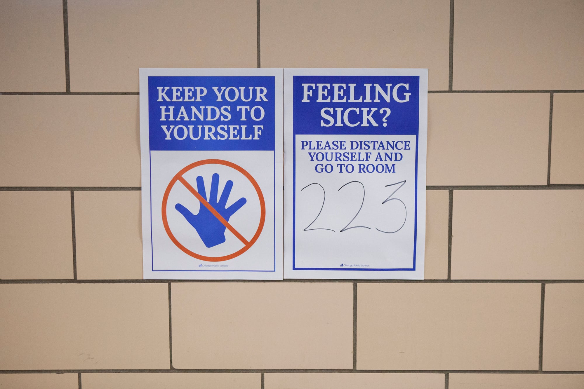 Posters in school hallway reminding students to keep their hands to themselves and stay distant if feeling sick.