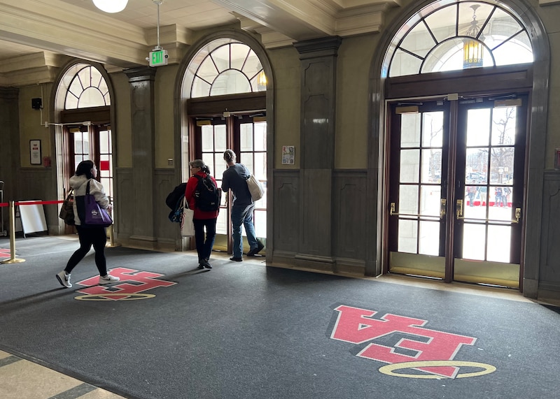 A couple of high school students walk toward the entrance of a school building on the inside.