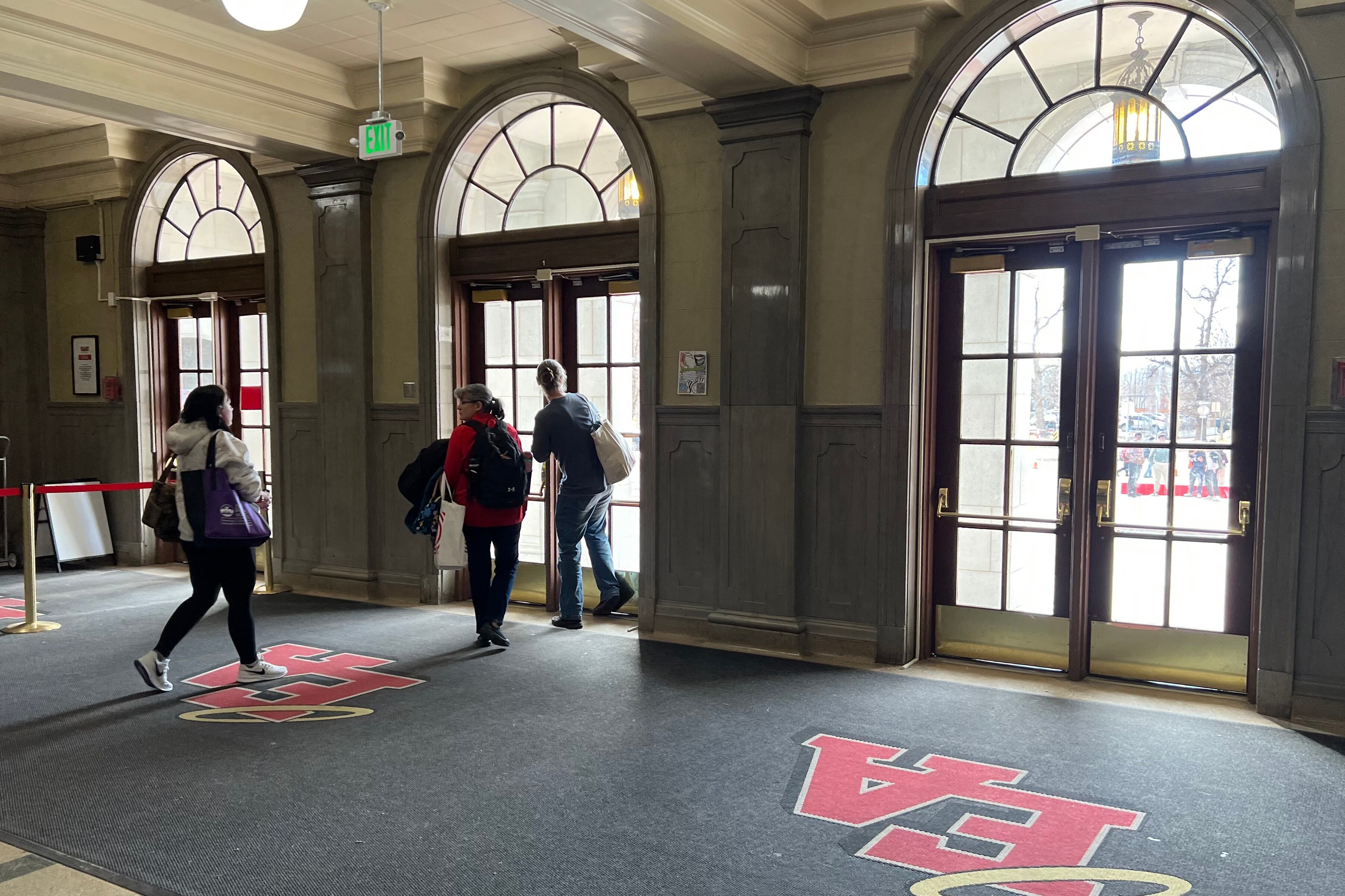 A couple of high school students walk toward the entrance of a school building on the inside.
