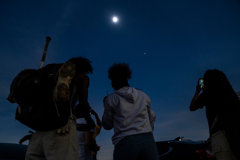A group of high school look up at the sky, which is completely dark because of a total solar eclipse.