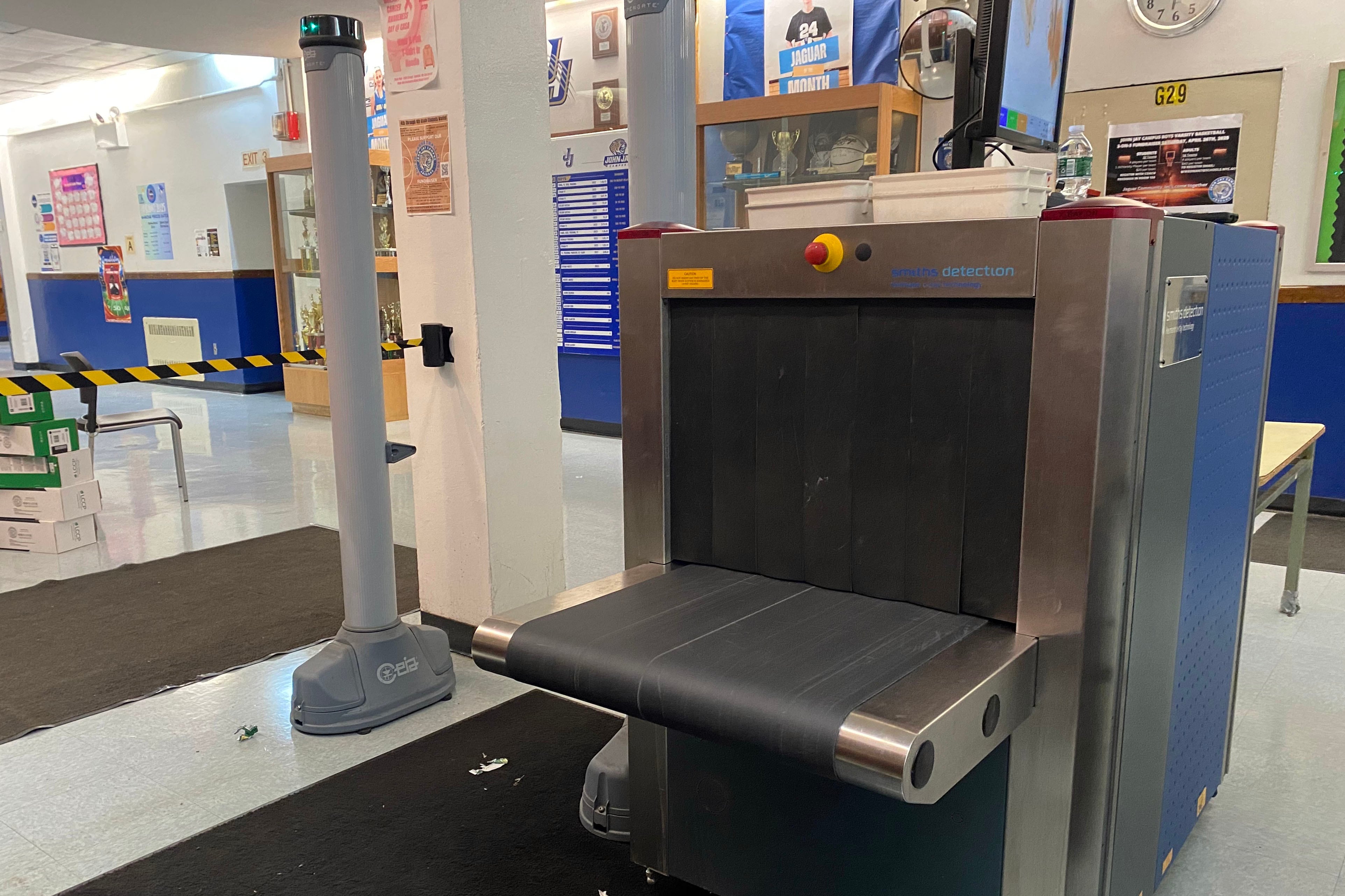 A large x-ray machine with a grey security poll in the background in a school lobby.