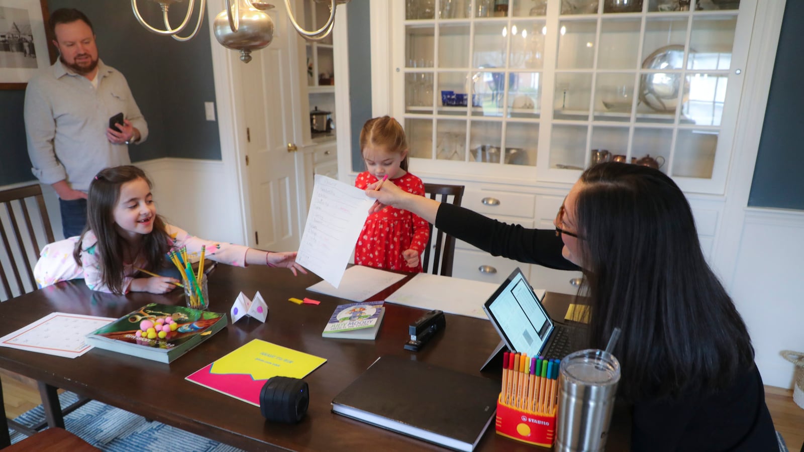 Sarah Yunits checks her daugher Ada's homework while Cora waits her turn as dad Conor Yunits is on a work conference call at their home in Brockton on March 19, 2020. Because of the coronavirus, the Yunits are able to perform their jobs at home and are home schooling their two children.