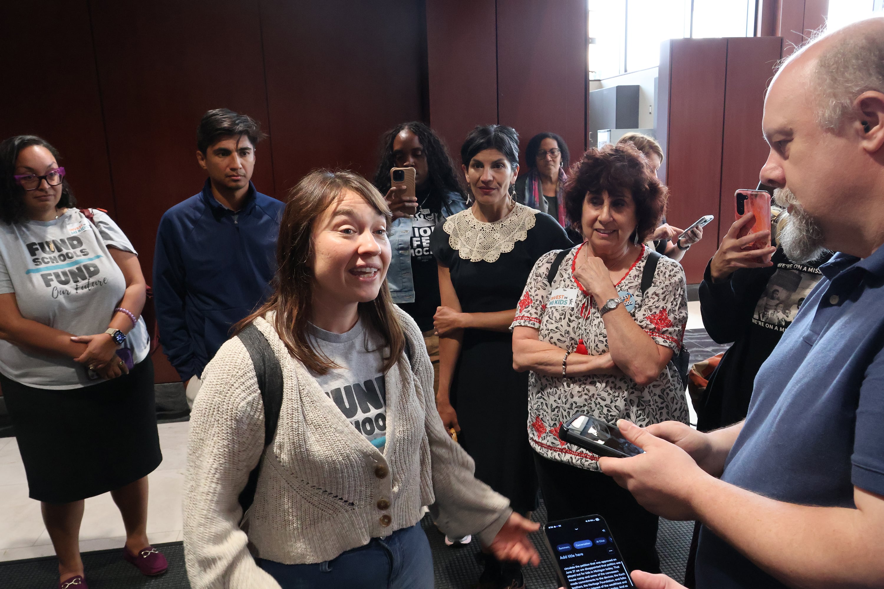 A photograph of a group of people talking in a hallway.