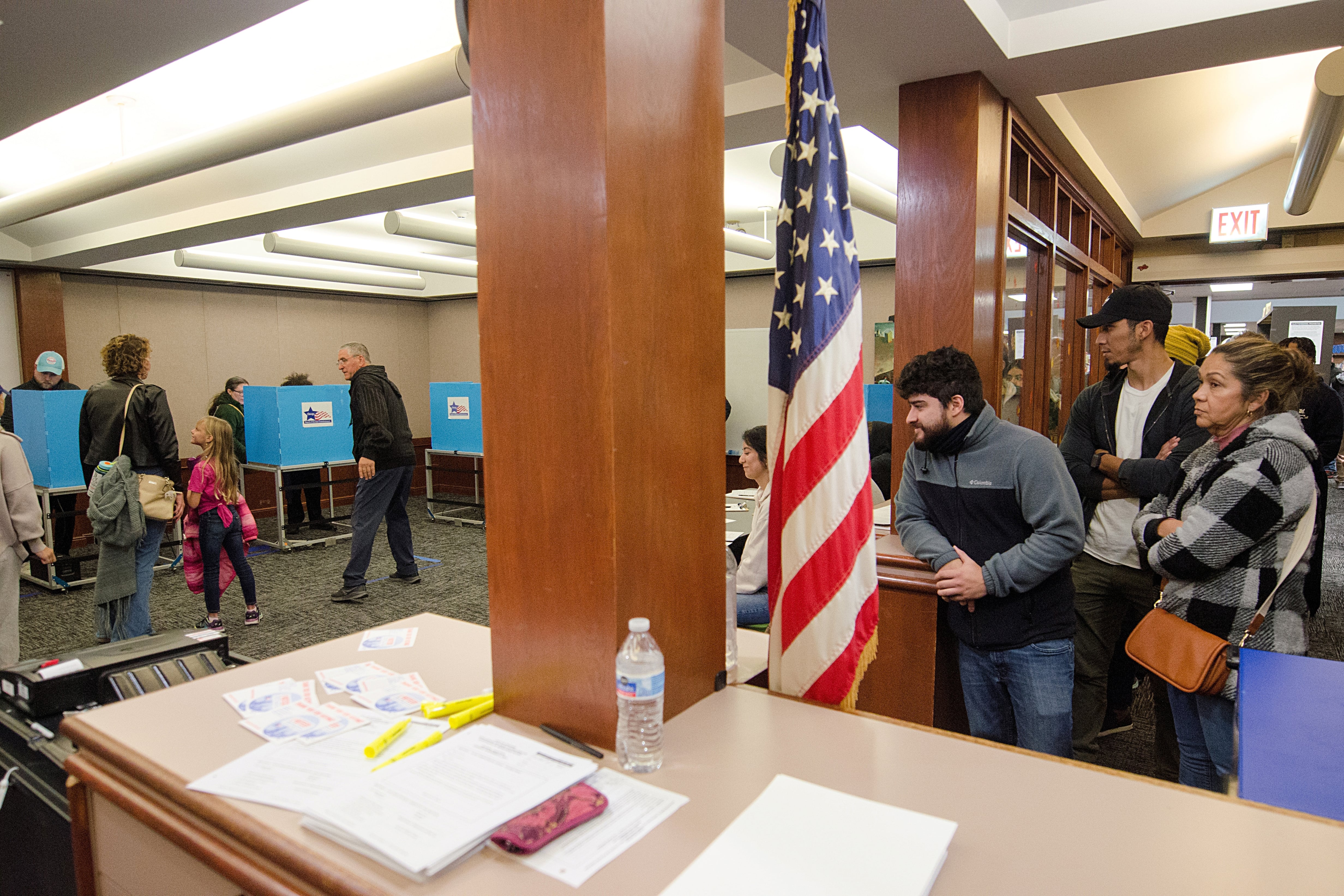 A room full of people either voting or waiting to vote with an American flag in the middle.