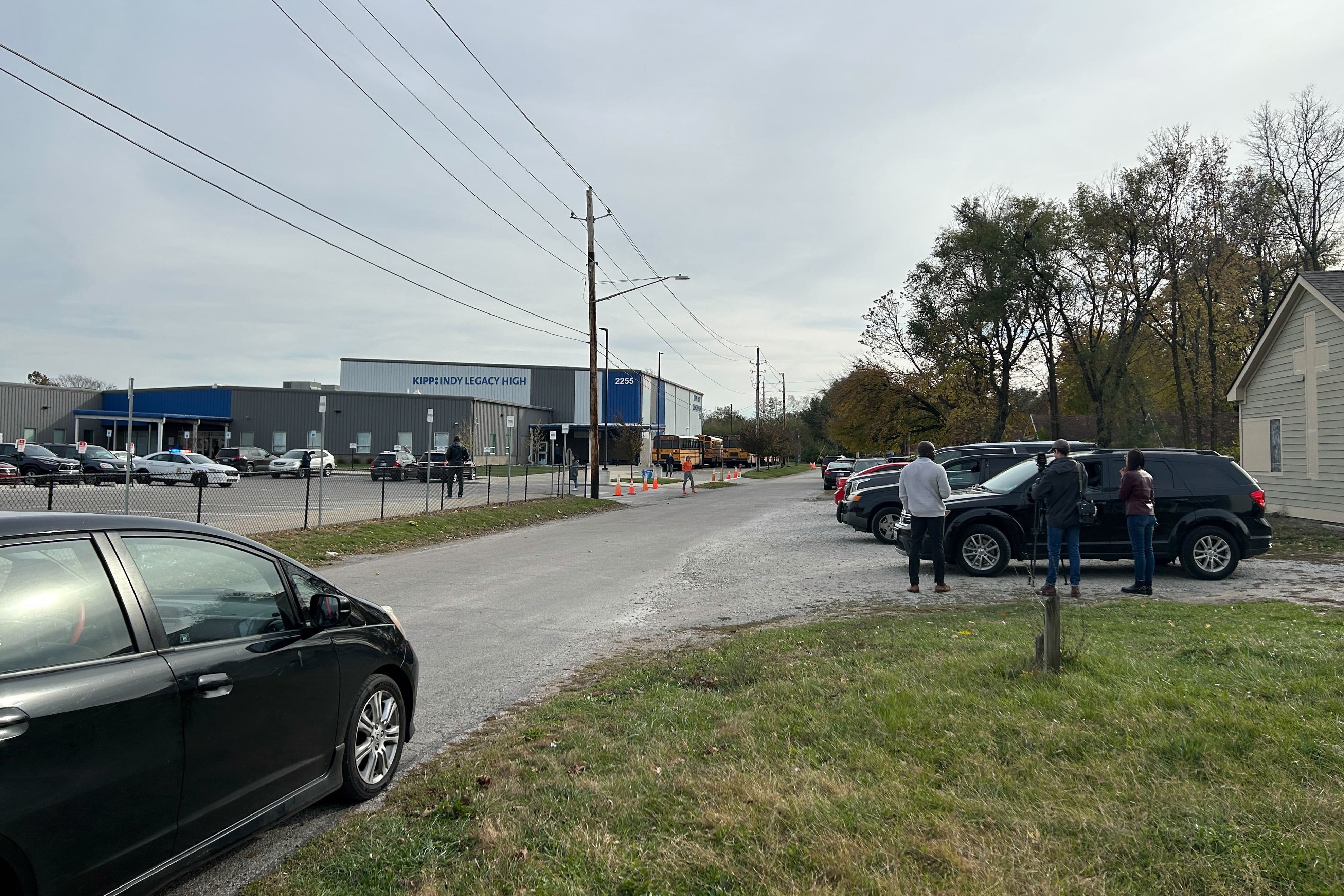 A building that says “KIPP Indy Legacy High” in the background, with cars and people standing near them in the foreground.