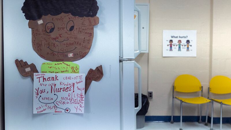 A poster of a little boy with a sign saying “Thank you nurses!” is on the side of the refrigerator in the nurse’s office of an elementary school.