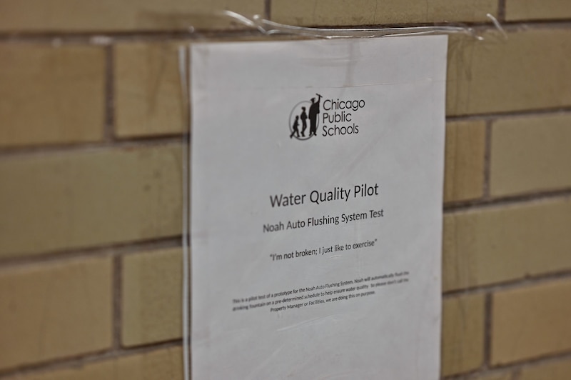A sign that says Water Quality Pilot taped to a tan brick wall.