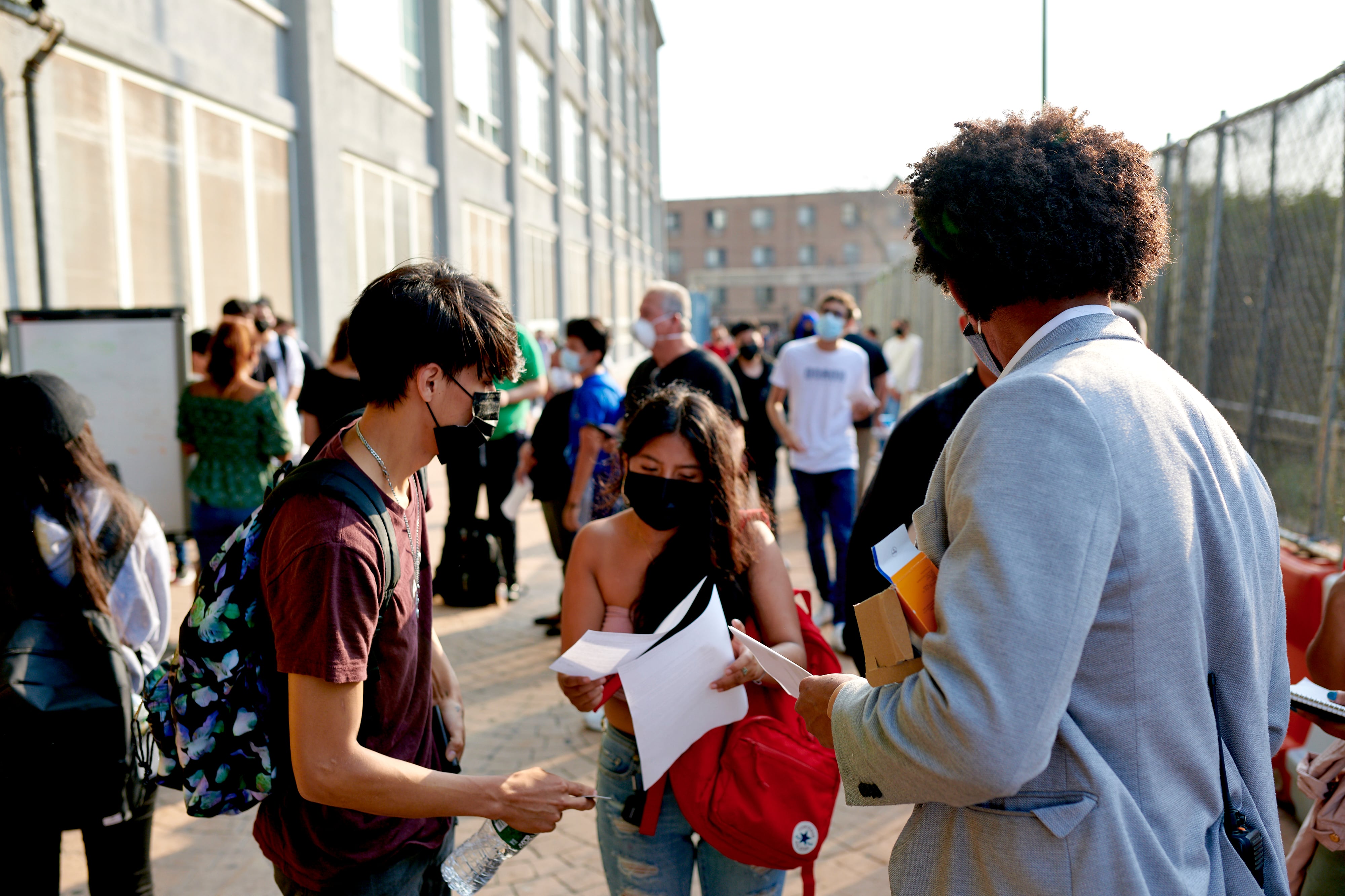 A group of students stand outside a school in New York City. They are holding paper forms.