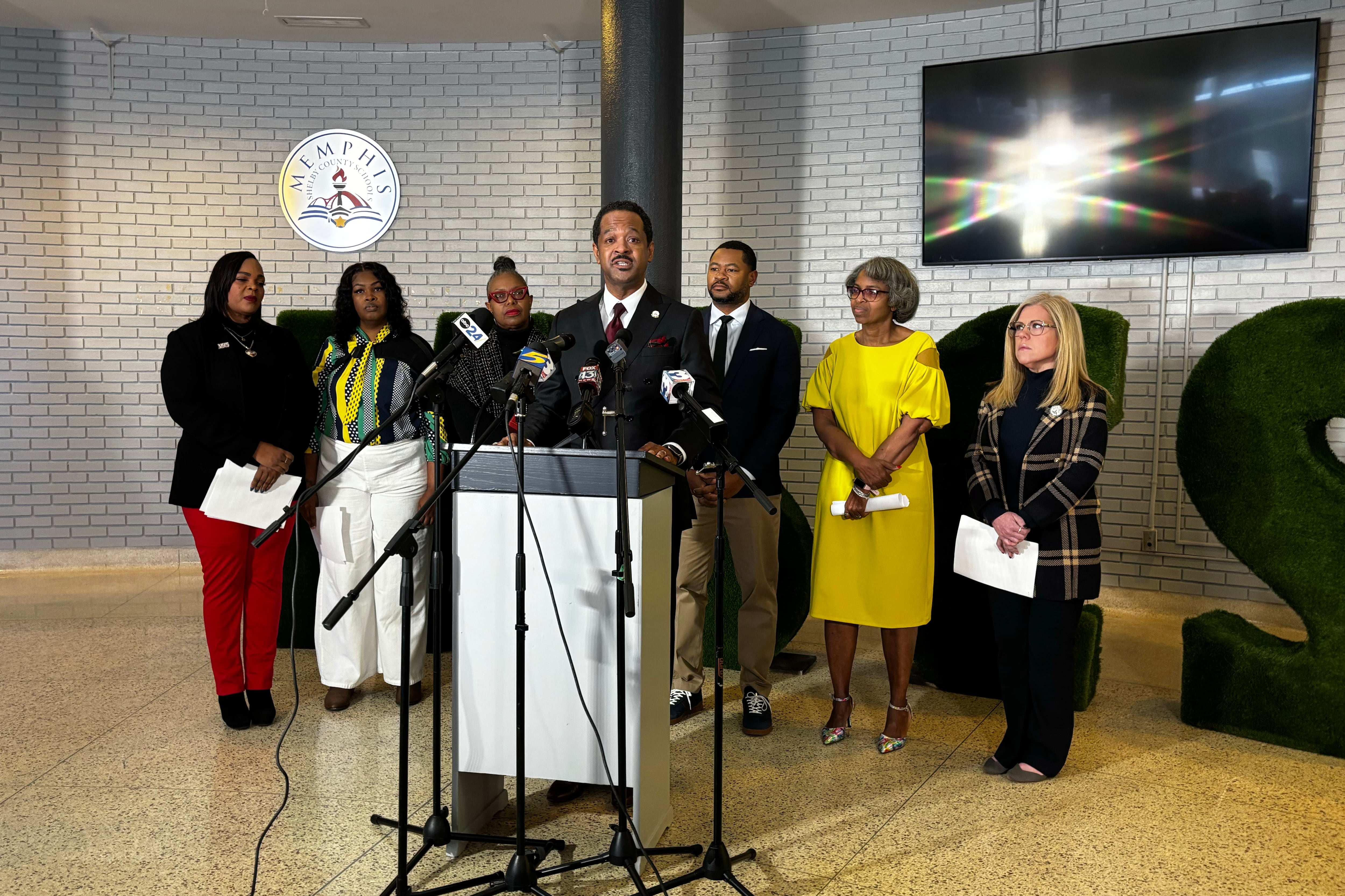 A group of people in business clothes stand behind a speaker at a podium in the lobby of a building.