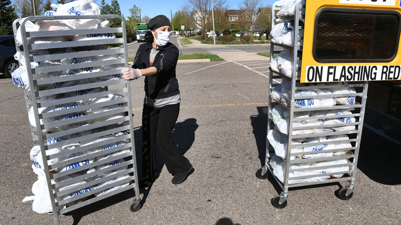A food service worker moves carts of food next to a school bus.