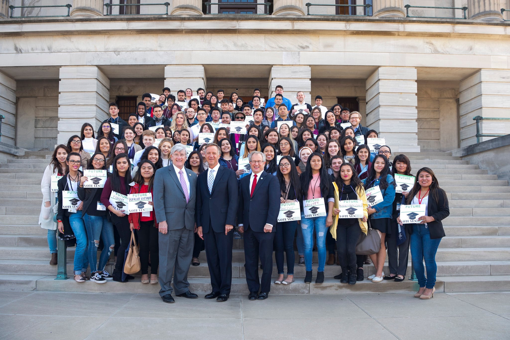 A large group of people pose for a portrait on a set of stairs in front of a large stone building.