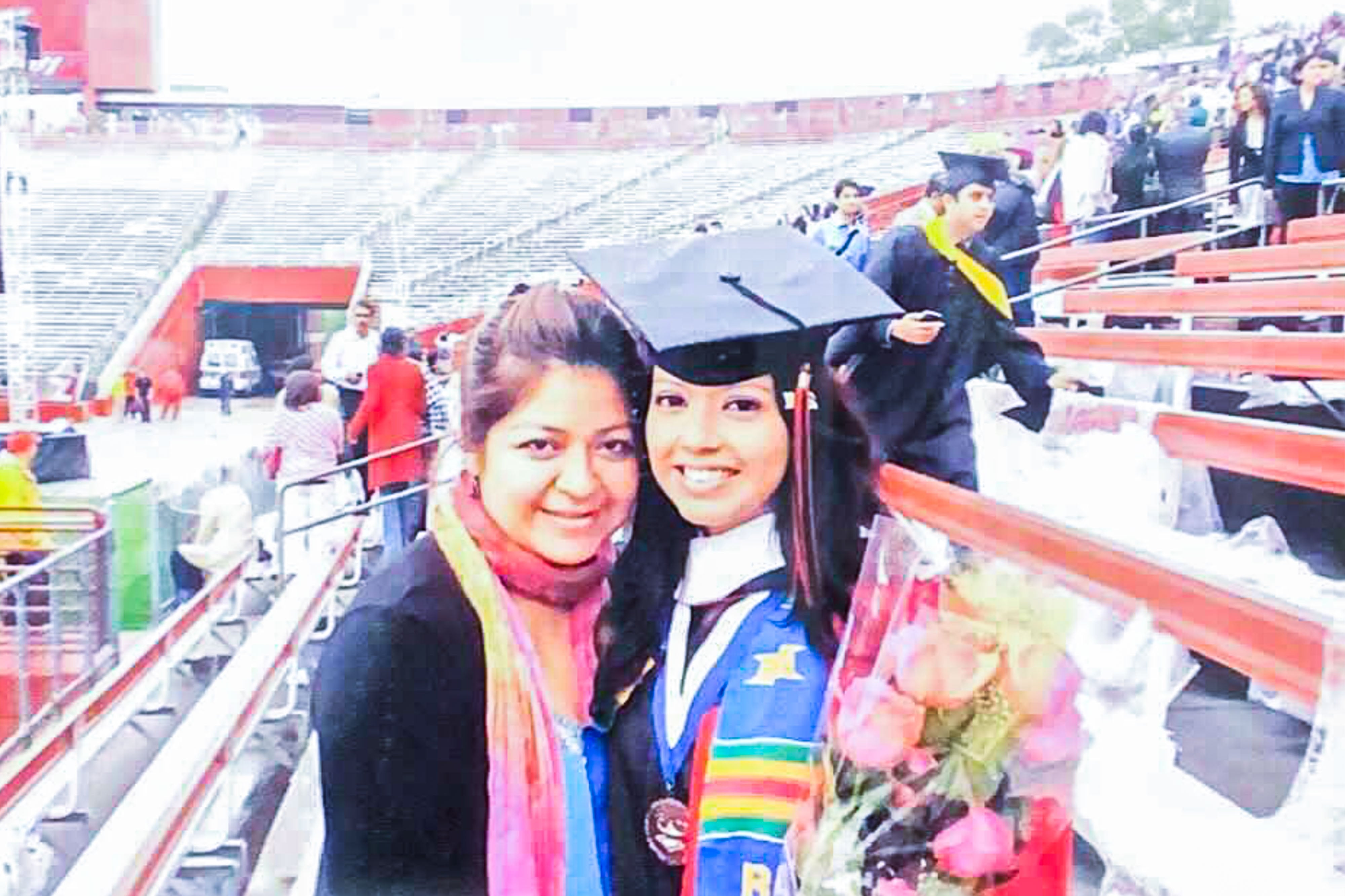 Chalkbeat Newark Bureau Chief Catherine Carrera  wears a black graduation cap and multicolored sash while posing with her mother at her college graduation.