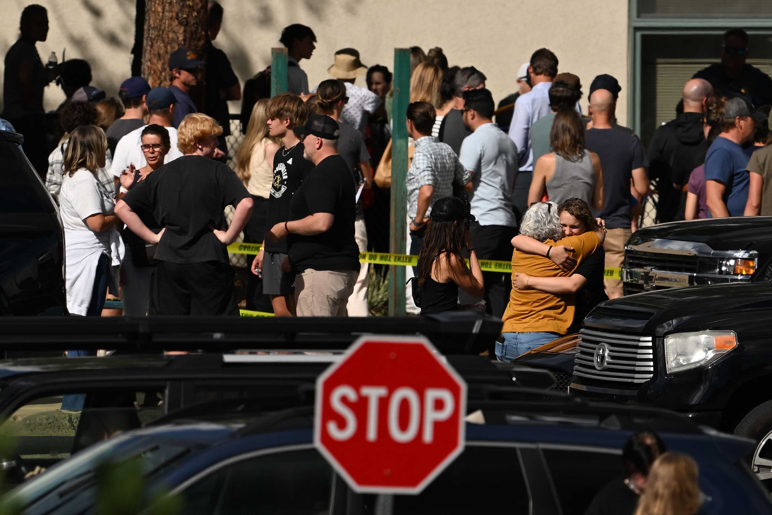 A photograph of a large group of teen students, family members and police outside of a school building.