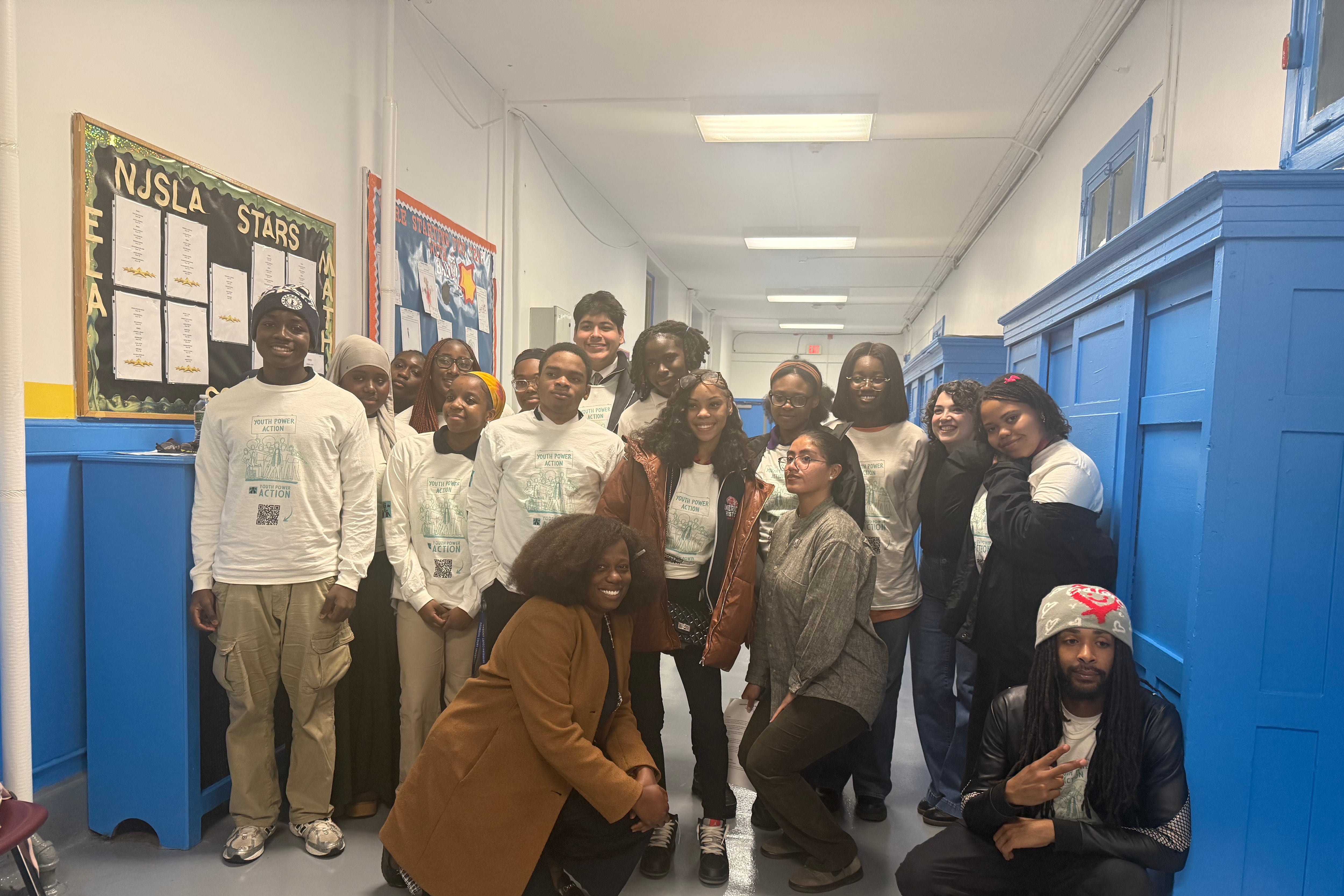 A group of students wearing white shirts is seen posing in a school hallway for a photo.