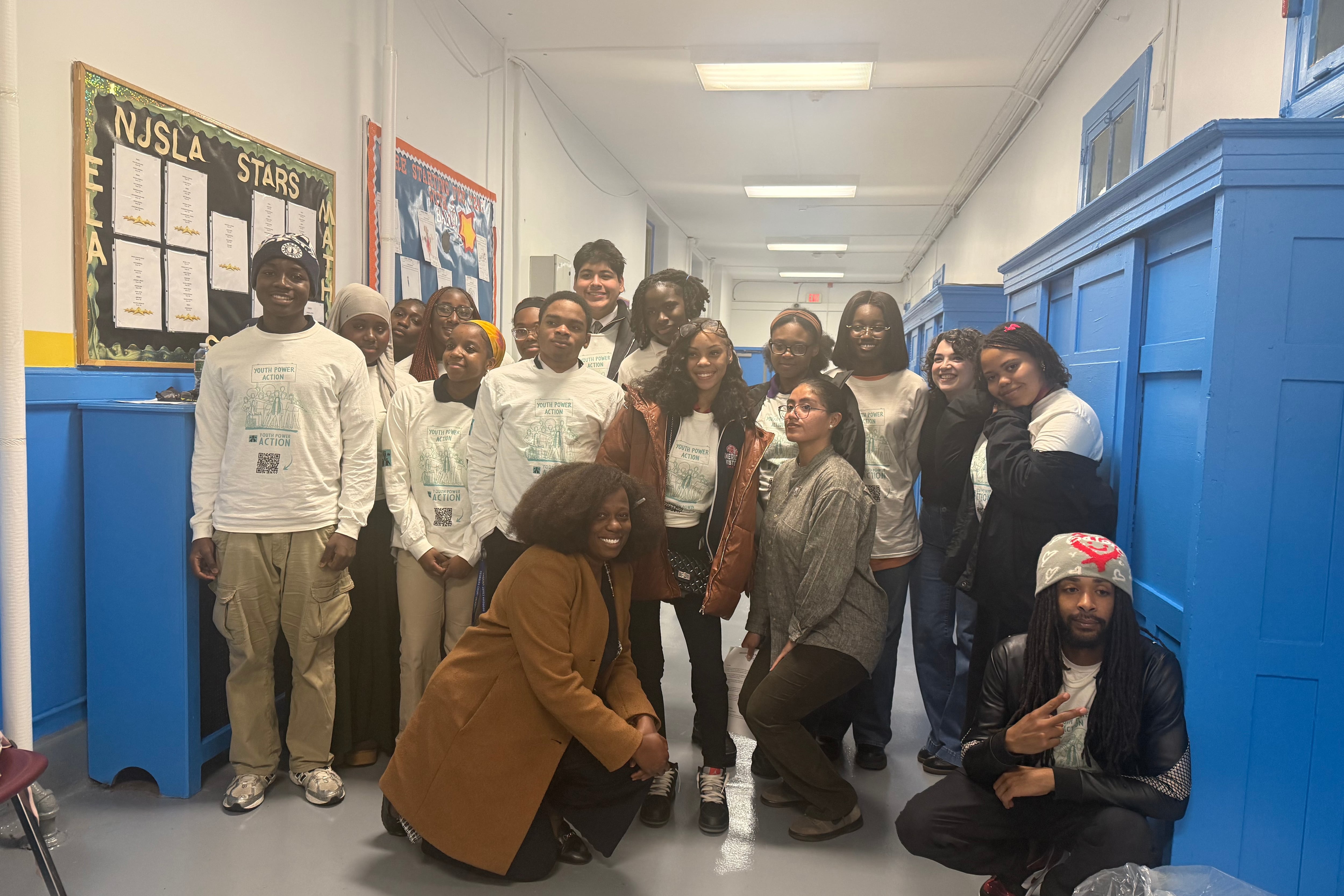 A group of students wearing white shirts is seen posing in a school hallway for a photo.