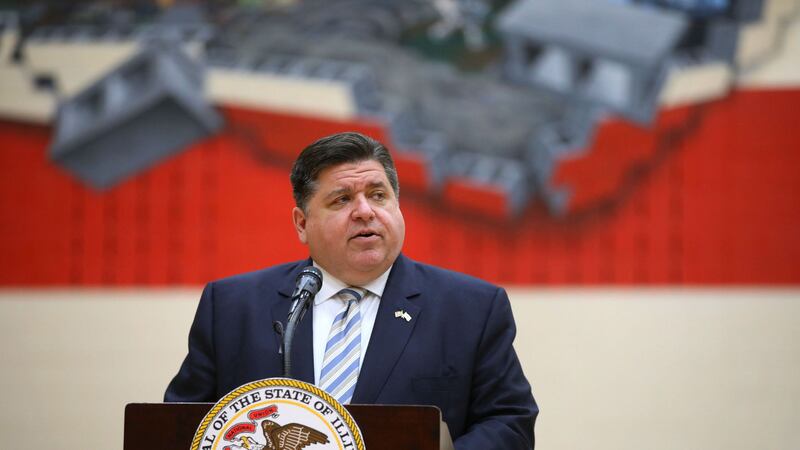 Illinois Governor J.B. Pritzker speaks at a podium in front of a large mural of the Illinois state flag.