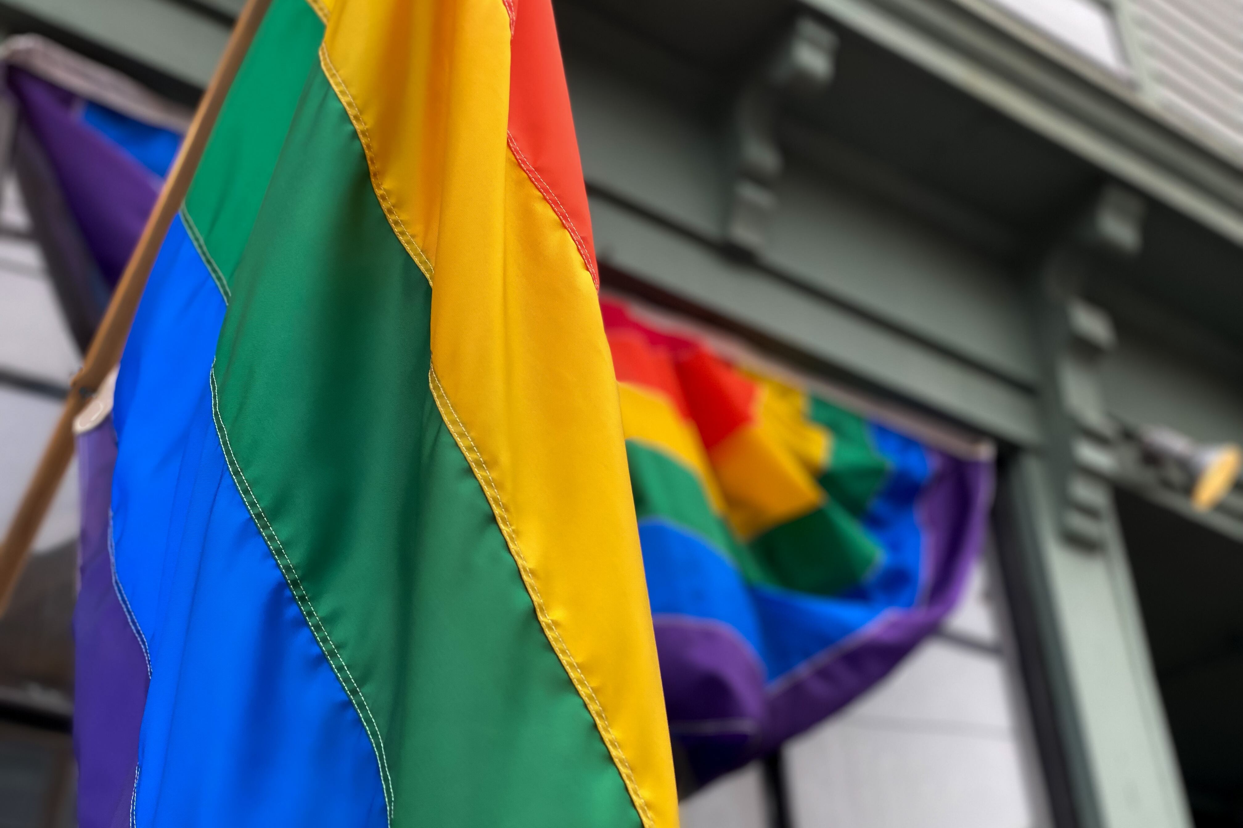 A Pride Flag hangs from a building, with a Pride banner on the window behind it.