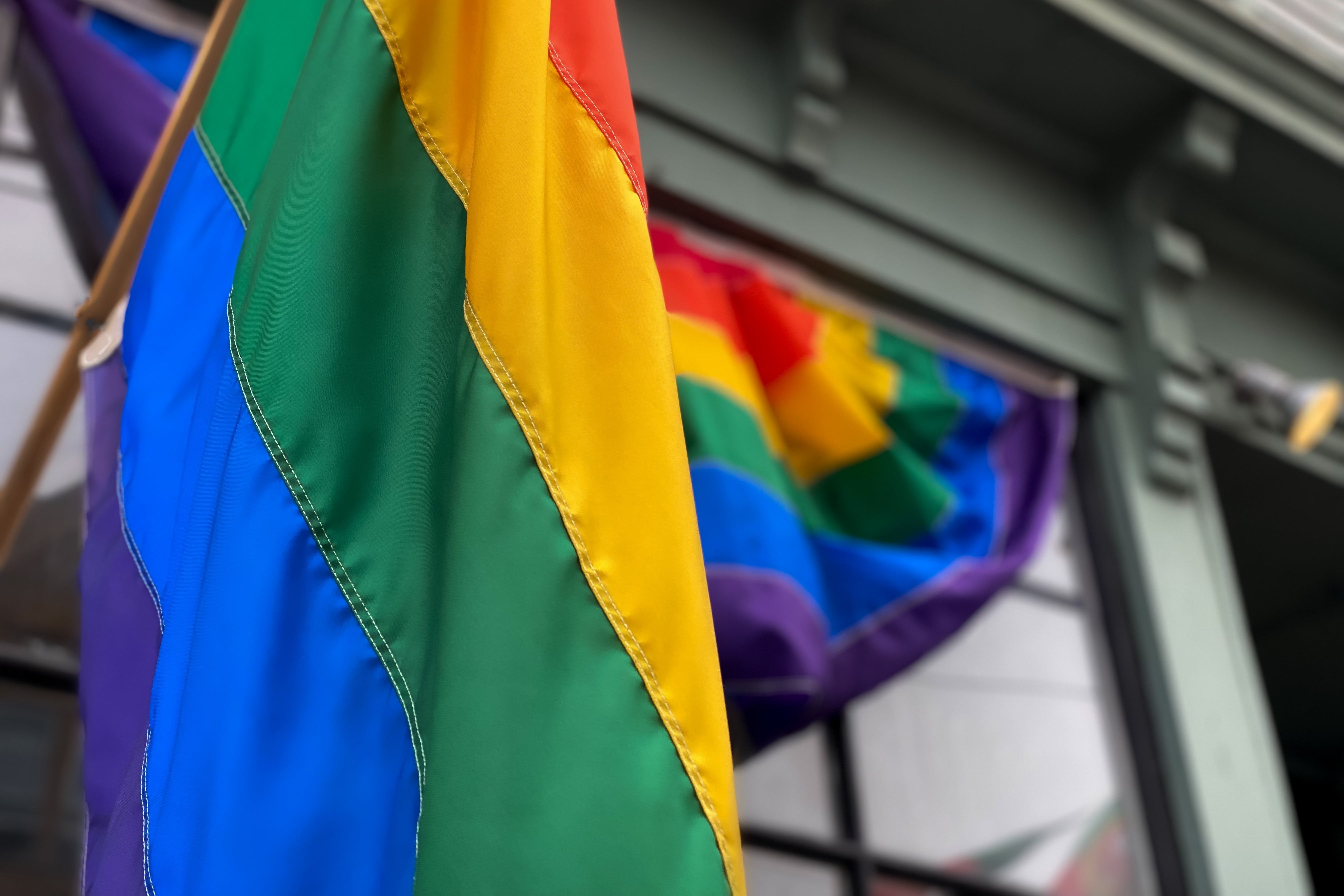 A Pride Flag hangs from a building, with a Pride banner on the window behind it.