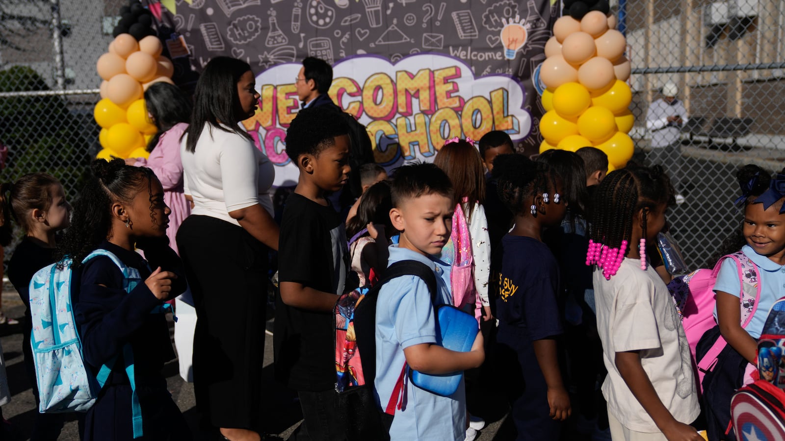 A group of kids with backpacks in front of a welcome back to school sign.