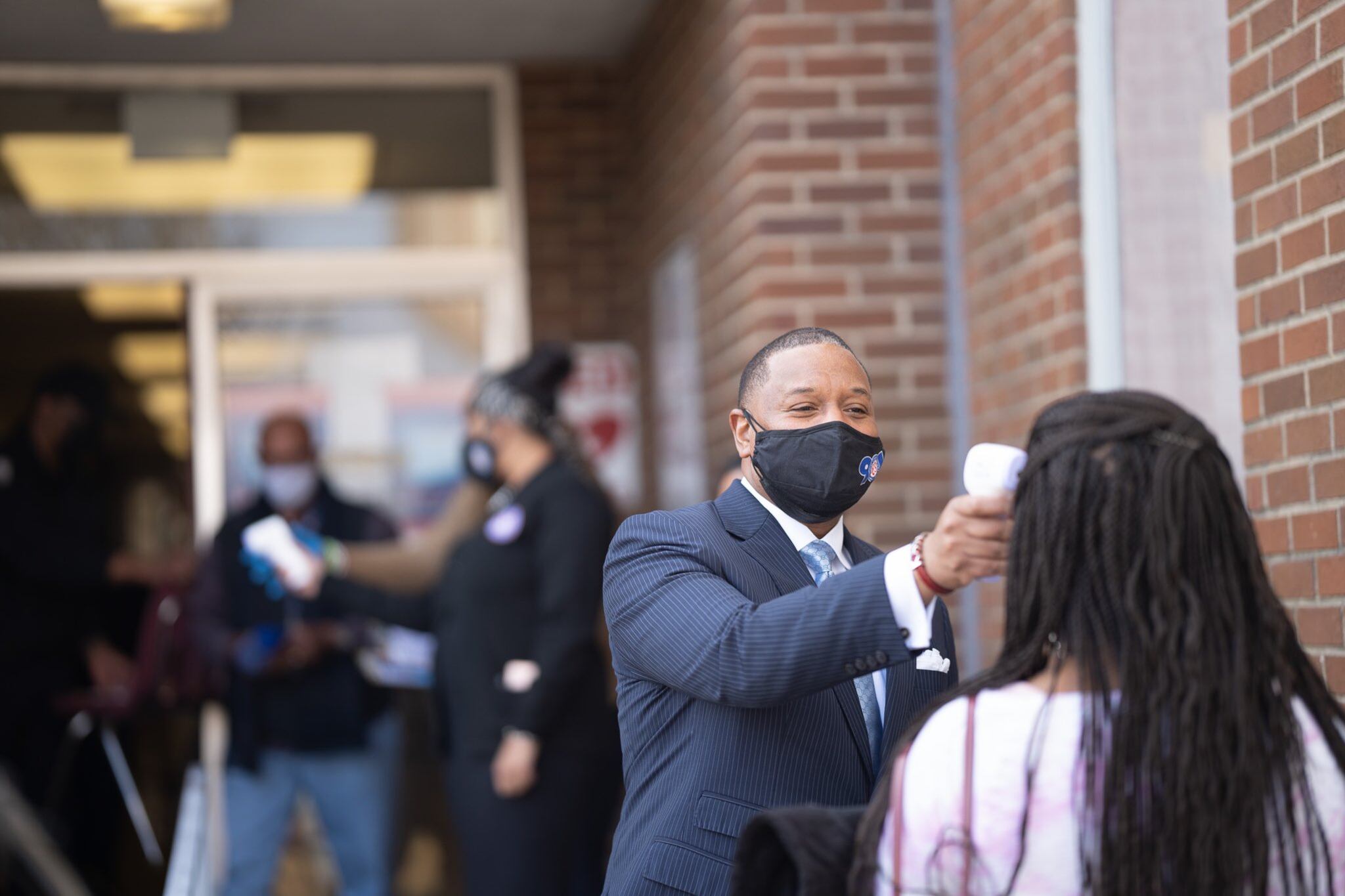 Superintendent Joris Ray uses a no-contact thermometer to screen a teacher before she receives a COVID-19 vaccine.