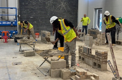 A group of students work on bricklaying in a warehouse.