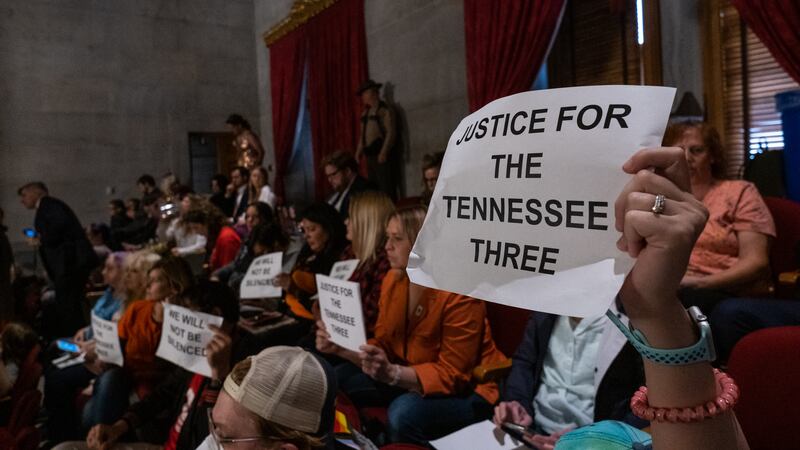 A hand holds onto an in-focus sign that reads Justice For The Tennessee Three in uppercase black letters on a landscape white piece of copy paper.