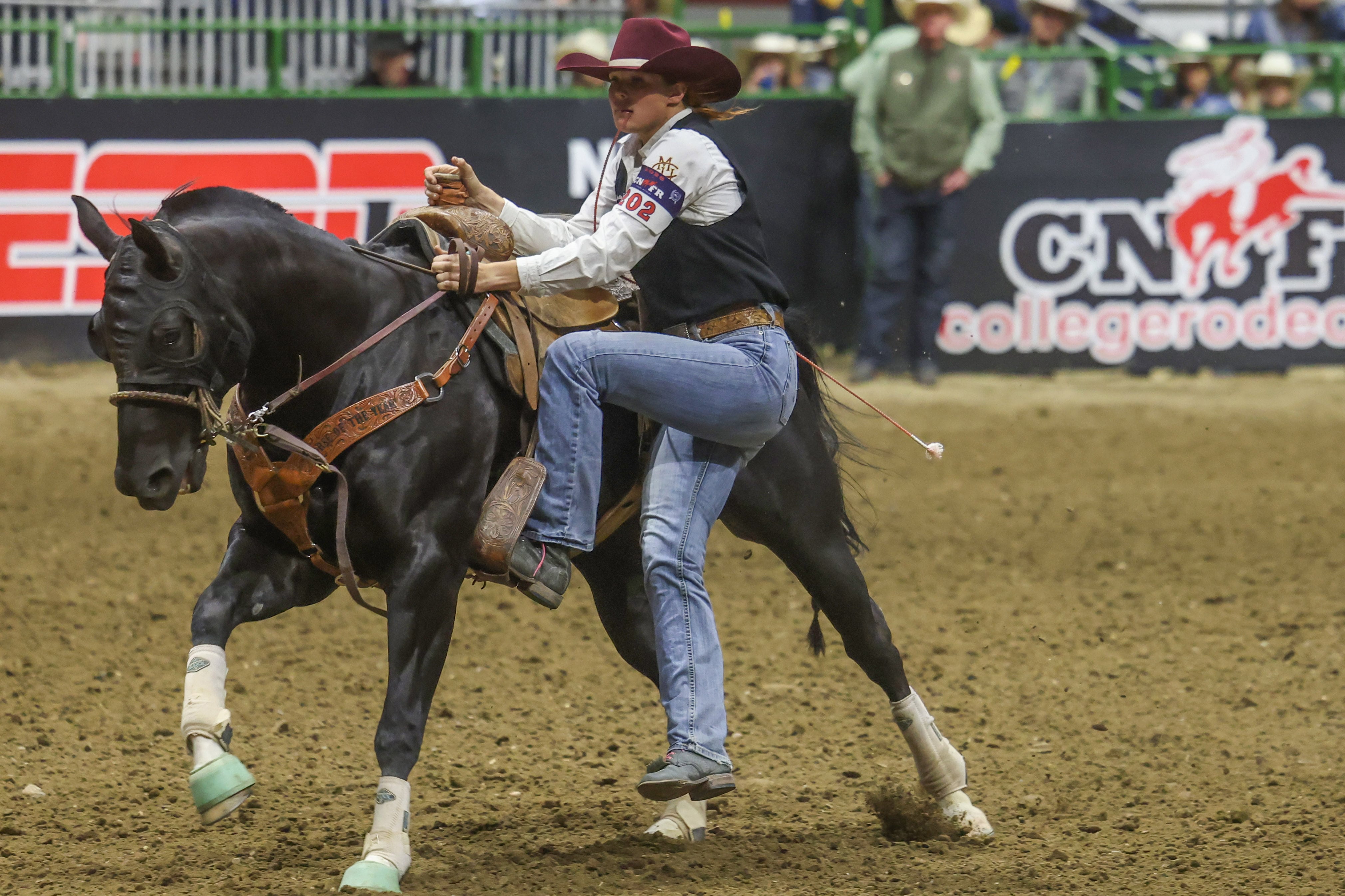 A photograph of a woman next to a horse during a goat tying competition for a college rodeo.