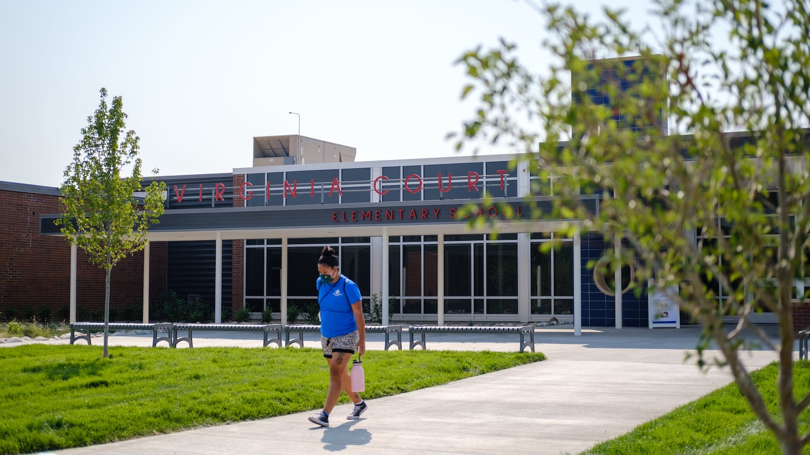 A woman in a blue shirt walks out of Virginia Court Elementary School on a bright summer day.
